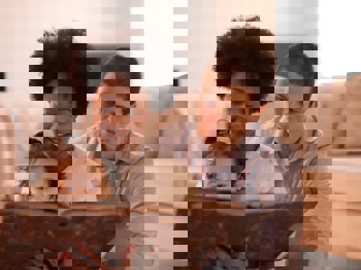 A man and a woman sit on the floor in front of a couch. They are reading to a toddler sitting in the woman's lap.