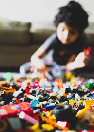 A child sits on the floor playing with a large pile of lego