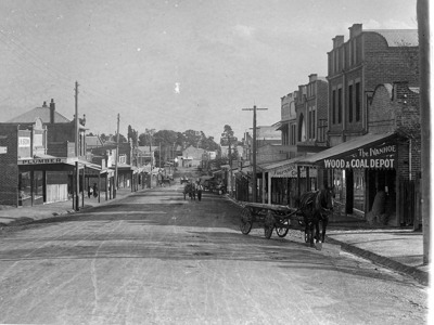 Heidelberg road, looking south, Ivanhoe. Wide dirt road, horse and cart, power lines and shops like plumber and wood and coal depot visible.