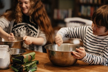 Two children are stirring ingredients in bowls on a kitchen counter