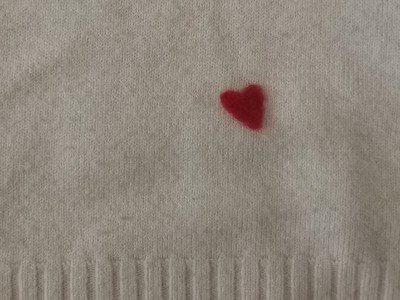 A photo of a small hole mended on a knit jumper using felting, the felt is made into a small heart